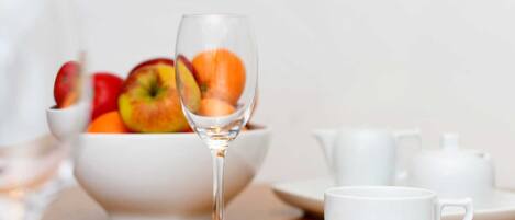 Un desayuno con un bol de fruta, una copa de vino y un juego de té blanco sobre una mesa de madera.