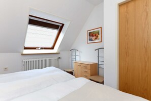 Quarto com claraboia, radiador, armário de madeira, mesa pequena e porta de madeira.