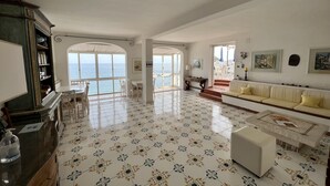 Un amplio salón con un gran ventanal con vistas al mar, un sofá blanco y un suelo de baldosas con un estampado floral.