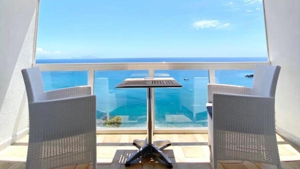 Un balcón con vistas despejadas al mar, una mesa y dos sillas de mimbre.