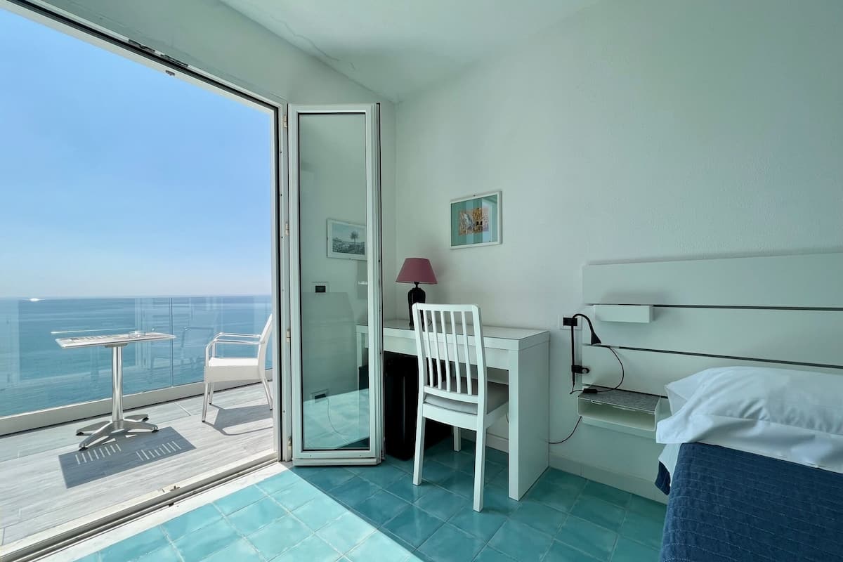 Une chambre d’hôtel avec un balcon, un bureau, une chaise, un lit et une vue sur la mer.