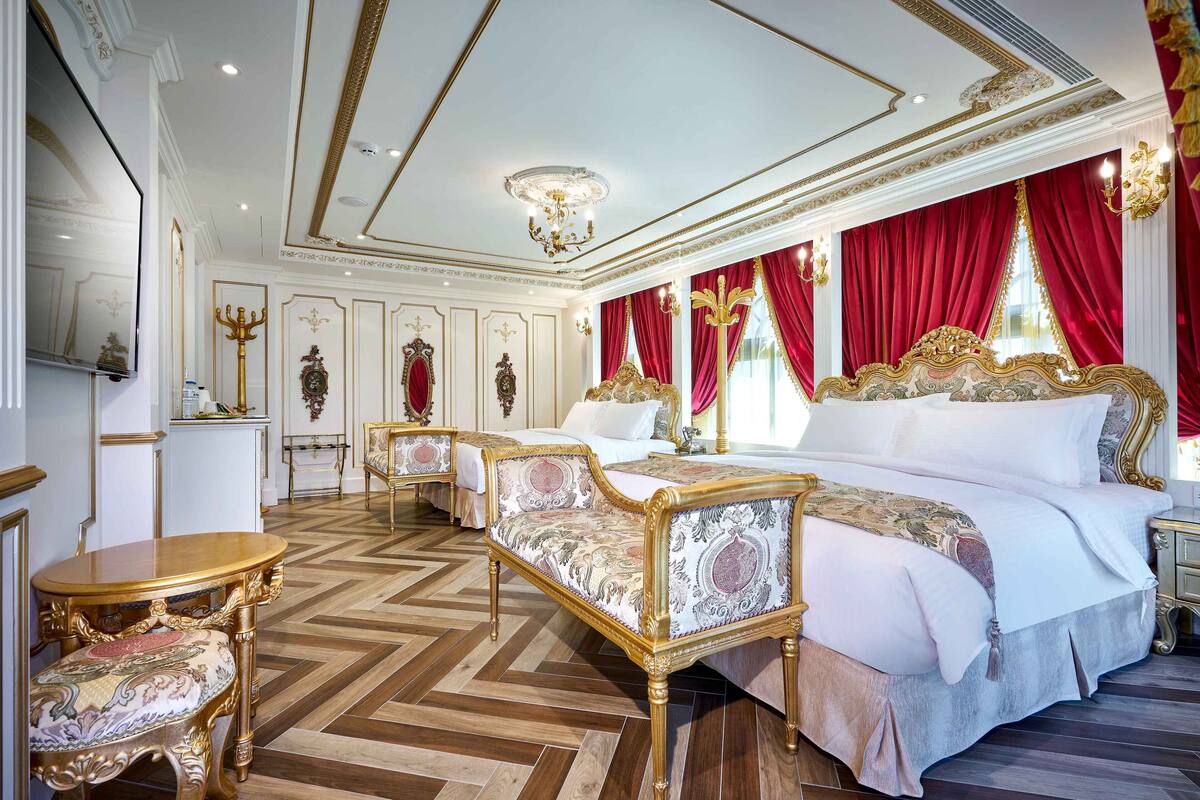 A luxurious bedroom with a large bed, ornate furniture, and a herringbone floor pattern.