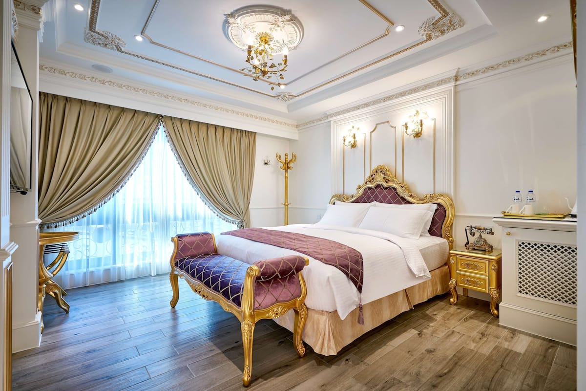 A luxurious bedroom with a large bed, ornate gold furniture, and a chandelier.