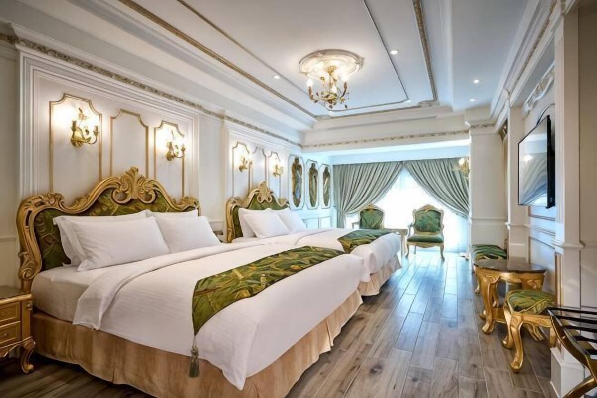 A luxurious hotel room with a large bed, two bedside tables, a TV, and a seating area with a chair and table.
