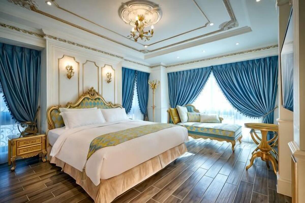 A luxurious bedroom with a large bed, a side table, and a chandelier.