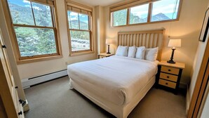 A bedroom with a large bed, two bedside tables, a nightstand, and three windows. - Great Location! Walk to Slopes, Dining, Shops! (Keystone)