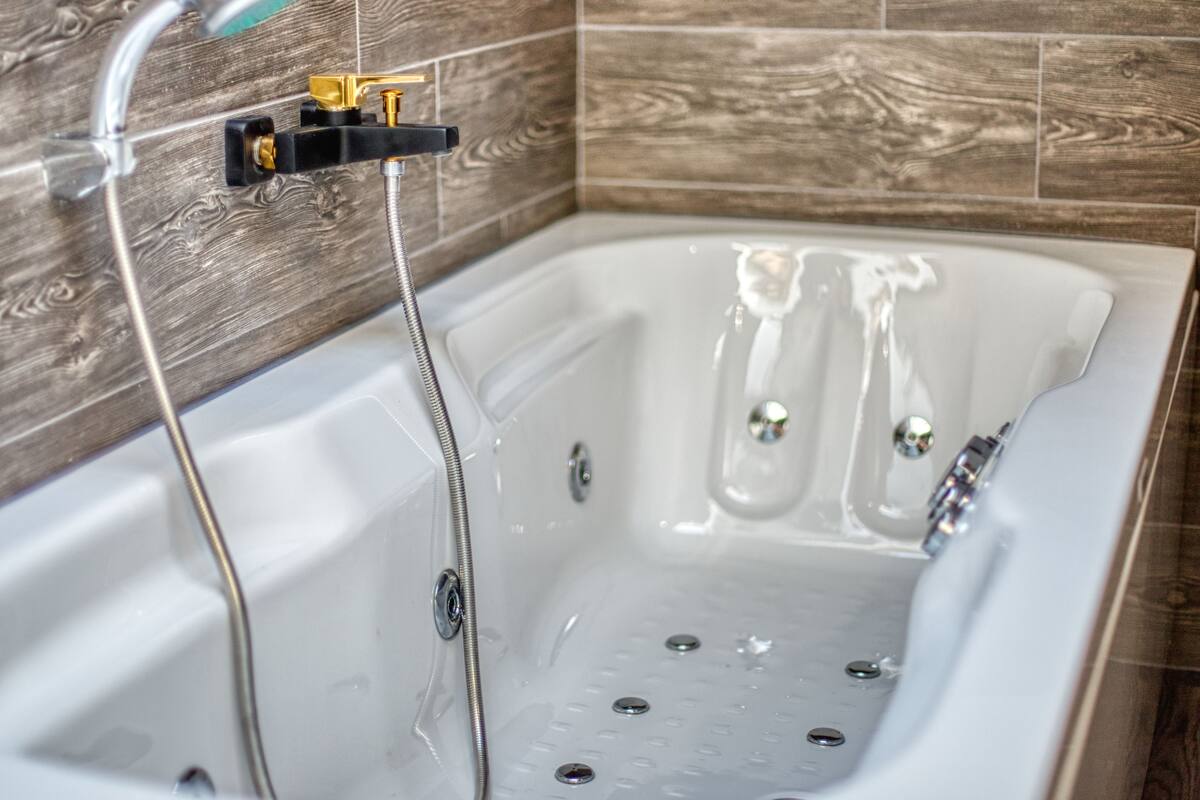 Une baignoire blanche, dotée d’une pomme de douche et d’un panneau de commande, est placée contre un mur en bois.