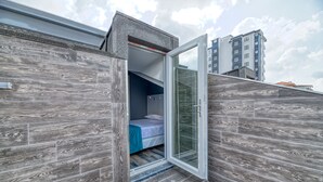 A compact bedroom with a sliding glass door leading to a balcony, wooden flooring, and a bed with a blue cover. - Grisverde Suites Hotel (Istanbul)