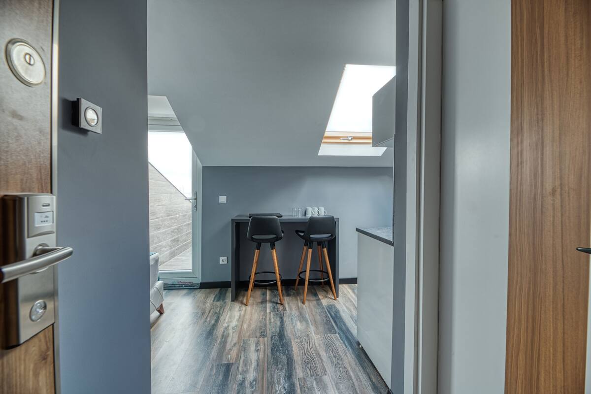 Un couloir étroit mène à une petite pièce dotée d’une lucarne, d’un bureau avec deux chaises et d’un plancher en bois.
