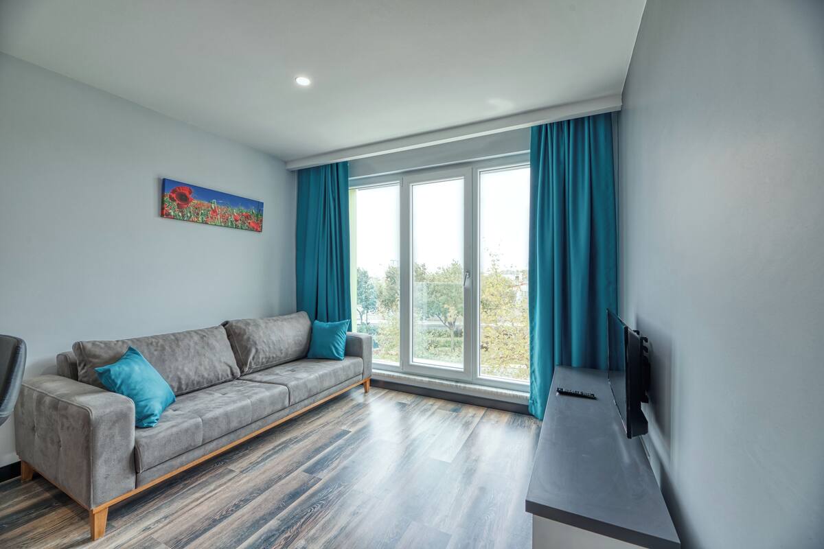 Un salon moderne avec un canapé gris, des rideaux turquoise et une grande fenêtre.