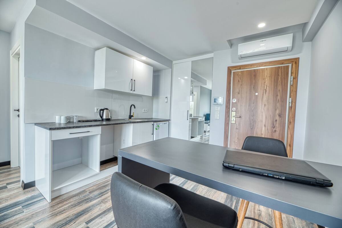 Une cuisine moderne avec des meubles blancs, un plan de travail gris et un ordinateur portable posé sur une table.