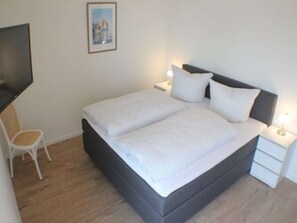 Una cama bien hecha con ropa blanca, una mesita de noche con una lámpara y una silla.