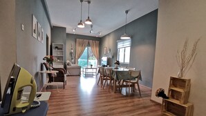 Un vaste espace de vie comprenant une table à manger, des chaises et un canapé. On y trouve également un ventilateur de plafond, des luminaires suspendus et une fenêtre avec des rideaux.