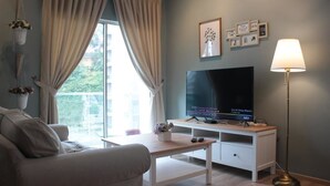 Un salon moderne avec un canapé, un téléviseur posé sur un meuble blanc, une lampe et une fenêtre avec des rideaux.