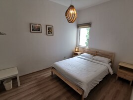 Une chambre à coucher avec un lit en bois, des tables de chevet, un banc et une fenêtre avec des stores.