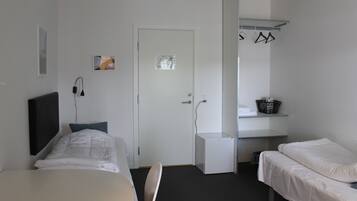 A room with two beds, a desk, a chair, a door, and a wall-mounted shelf with clothes.