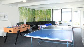 A room with a foosball table, ping pong table, and a sofa.