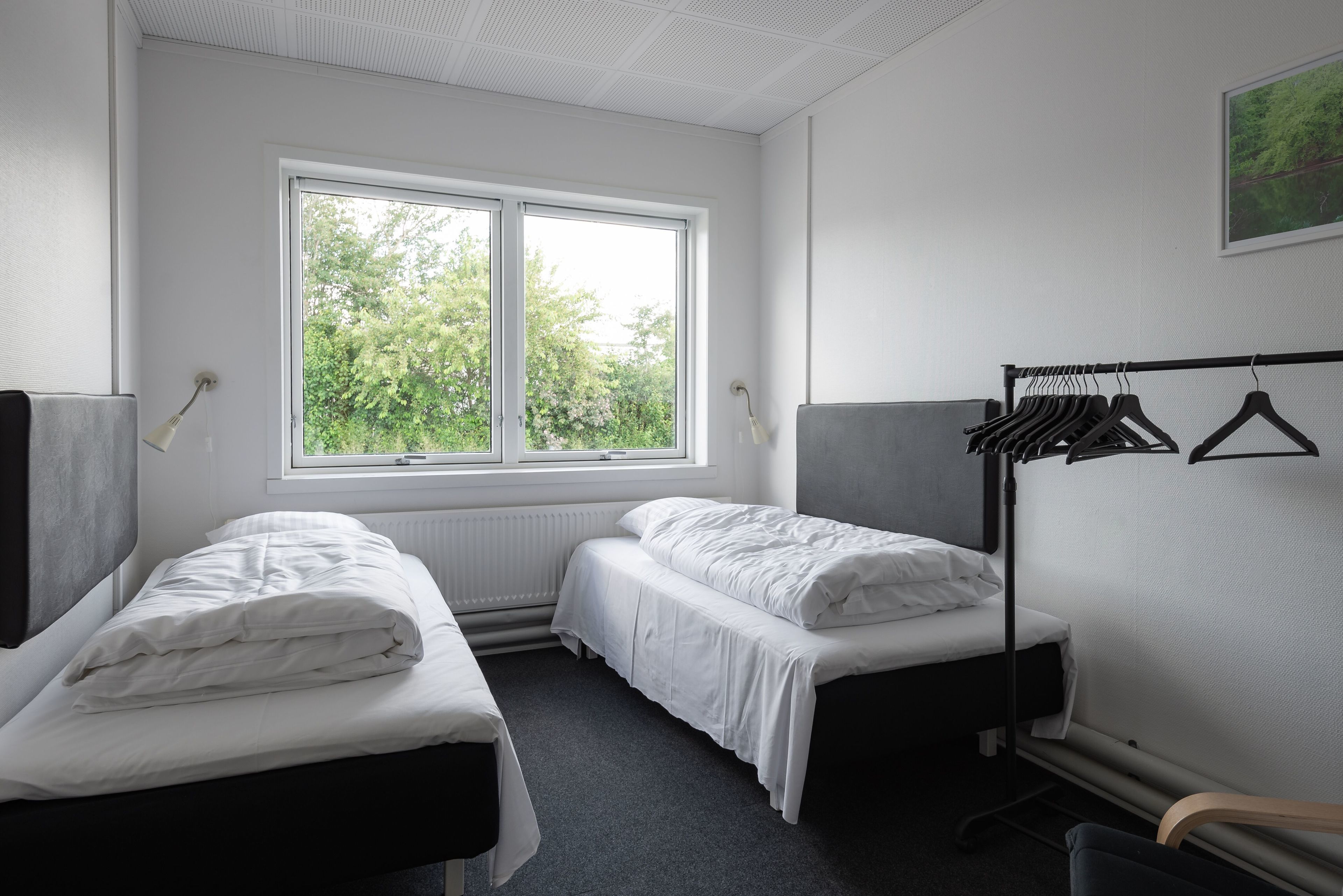 A room with two beds, a window, and a coat rack.