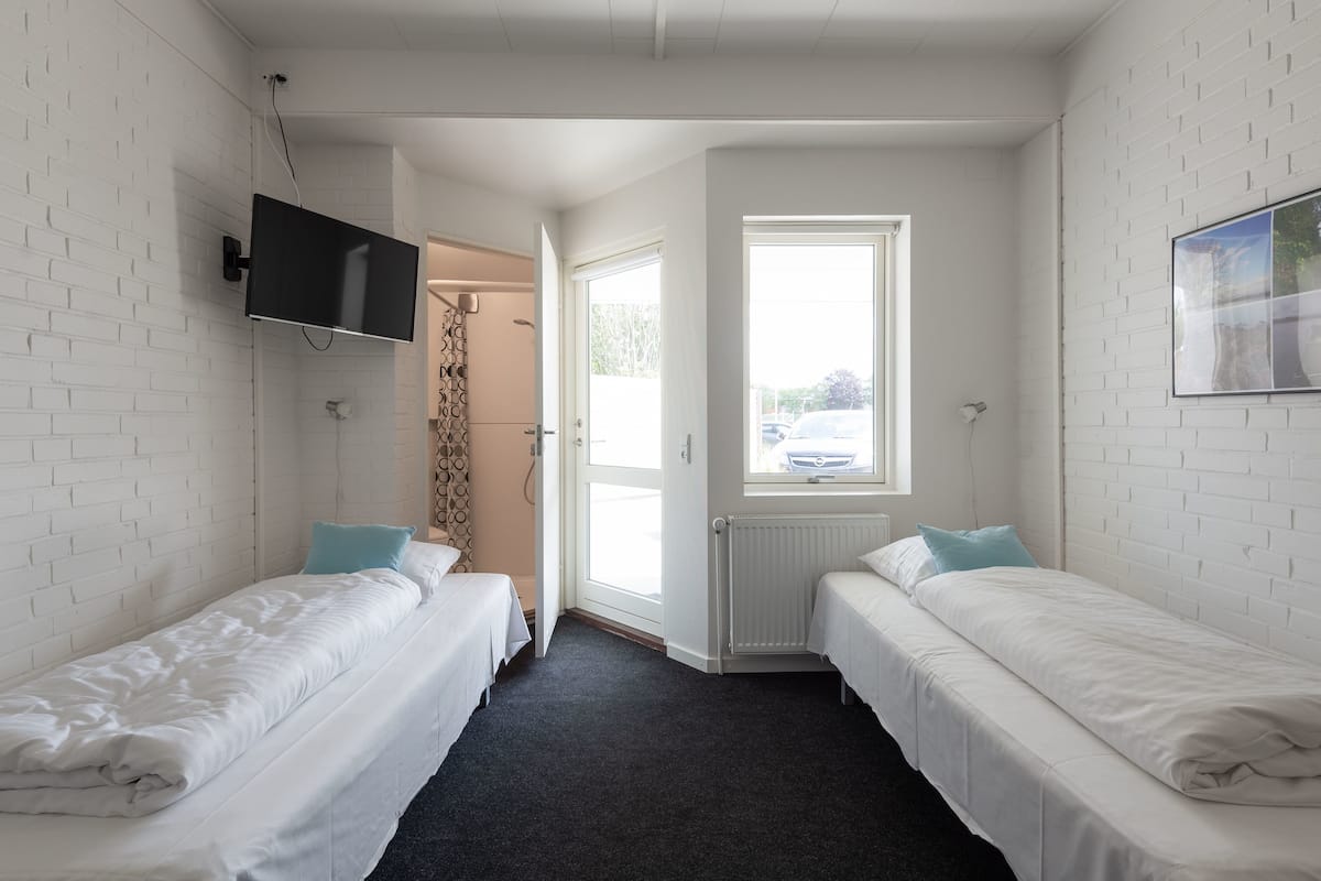 A small, clean room with two beds, a TV, a window, and a radiator.