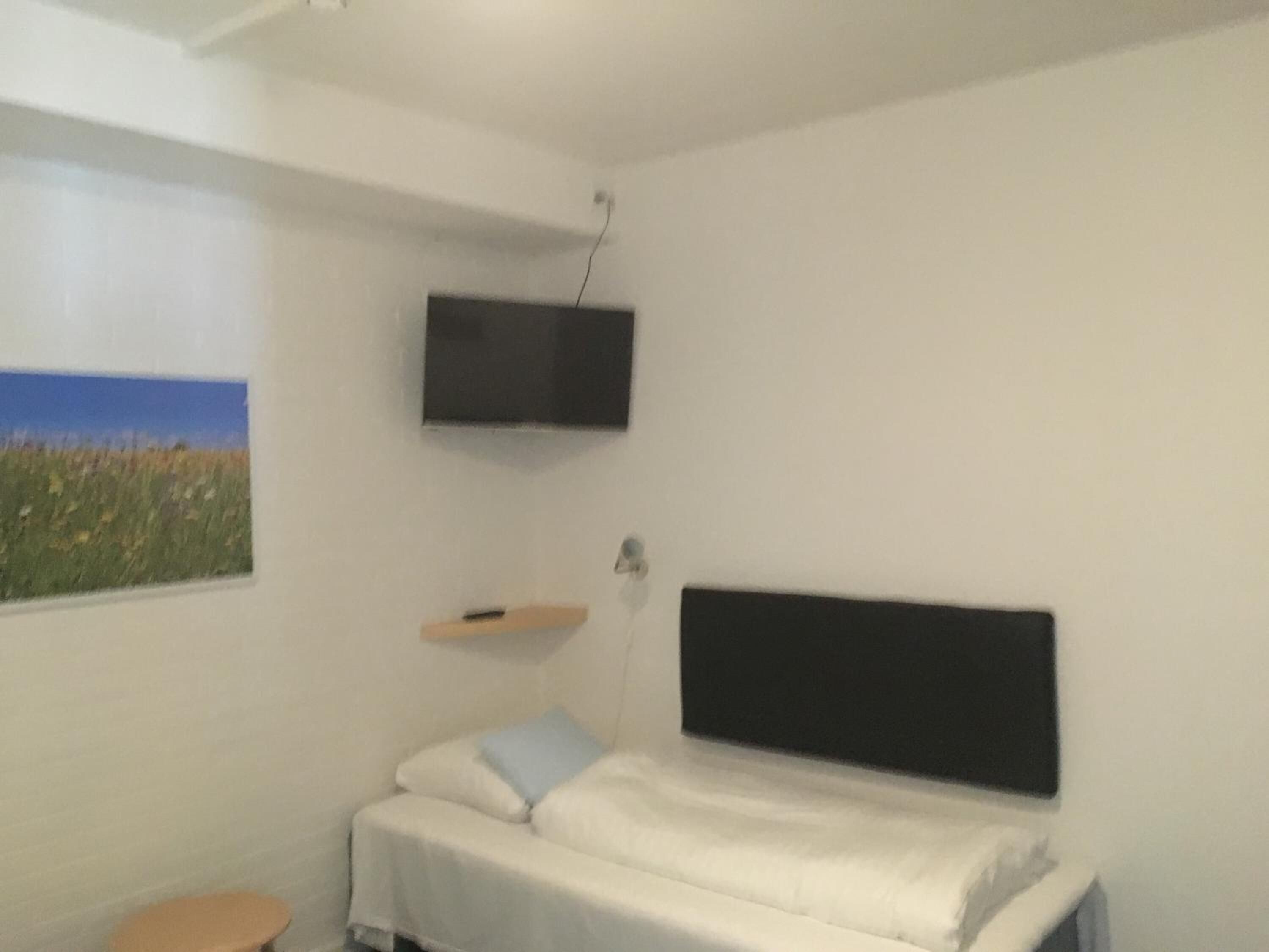 A small, simple room with a bed, a TV mounted on the wall, and a window with a view of a field.