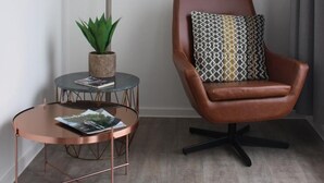 A modern room with a brown leather chair, a small round table with a lamp, and a potted plant. - Citystay (Antwerp)