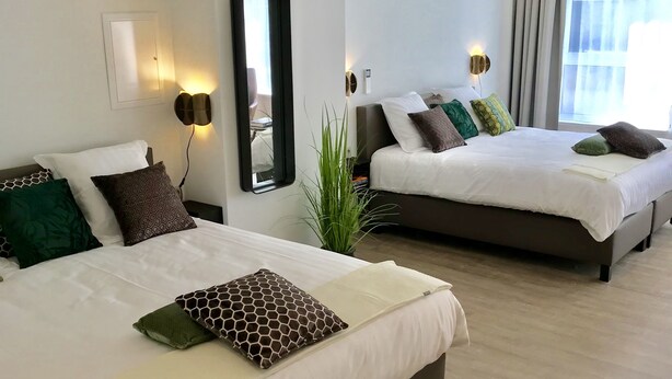 A hotel room with two beds, a large mirror, wall sconces, and a potted plant. - Citystay (Antwerp)