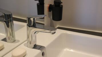 A modern bathroom with a chrome faucet, a soap dispenser, and a black soap bottle.