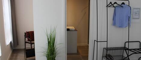 A room with a potted plant, a chair, a clothing rack with a shirt, and a door leading to another room.