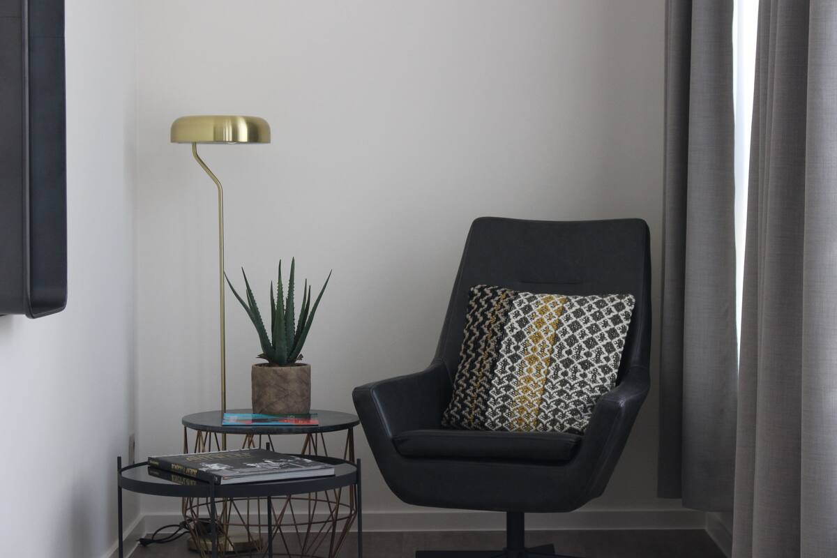 A corner room with a black leather armchair, a small round table with a potted plant, and a floor lamp.