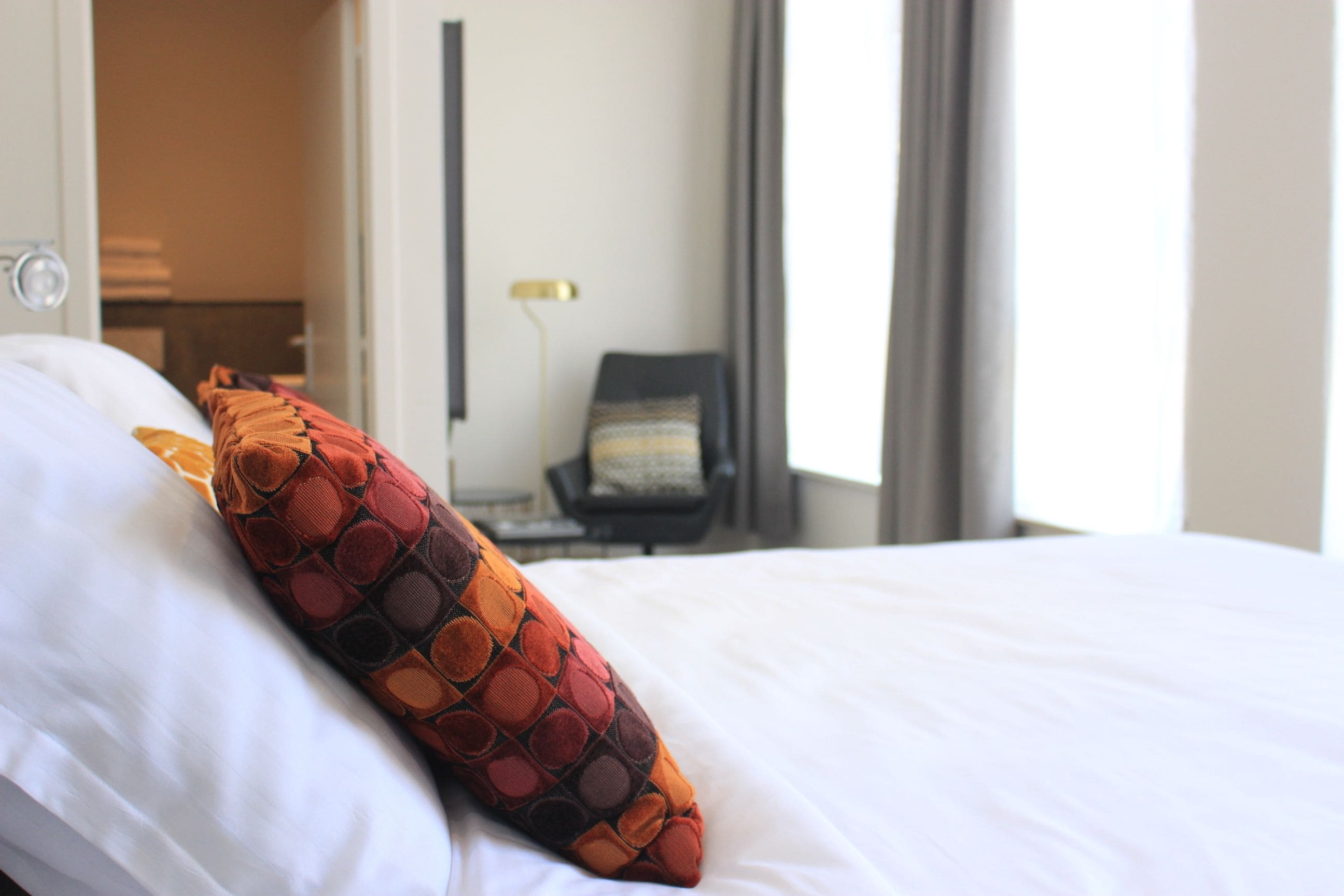A hotel room with a bed, a chair, and a lamp.