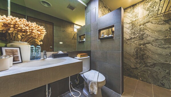 A modern bathroom with a marble wall, a sink with a vase of flowers, and a toilet with a towel.