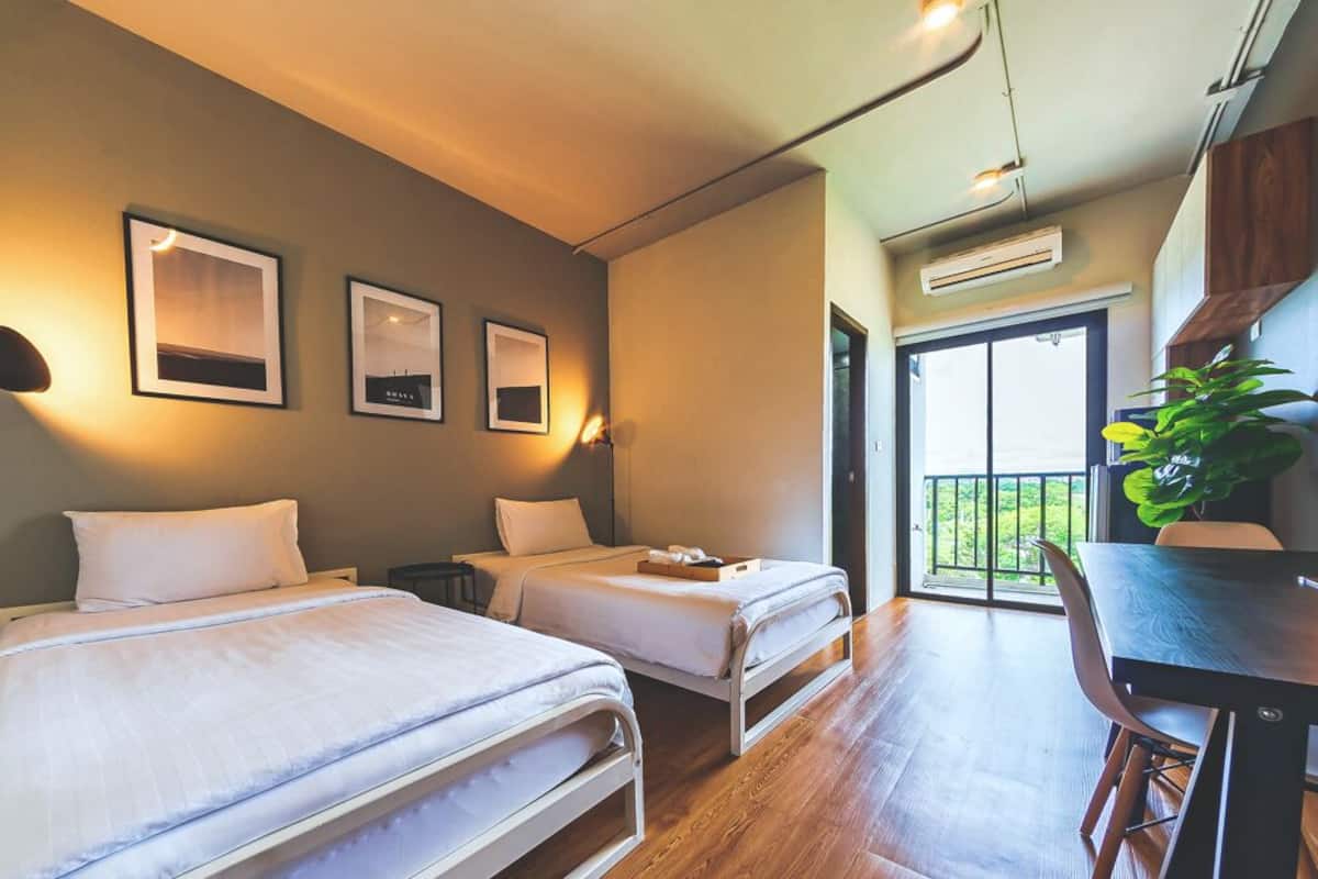 Ein Hotelzimmer mit zwei Betten, einem Esstisch und einem Balkon mit Pflanze.