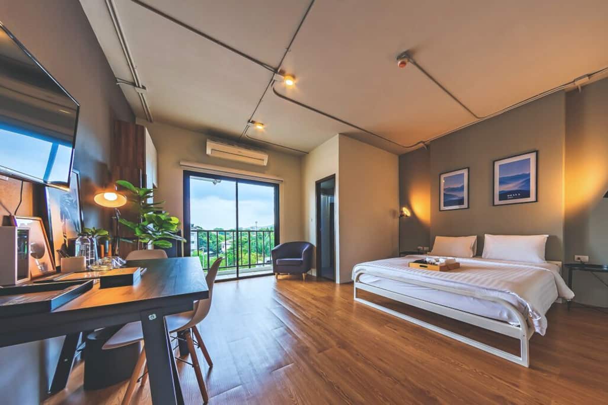 Ein modernes Schlafzimmer mit einem großen Bett, einem Schreibtisch und einem Stuhl. Ein Fenster bietet Blick auf grüne Natur.