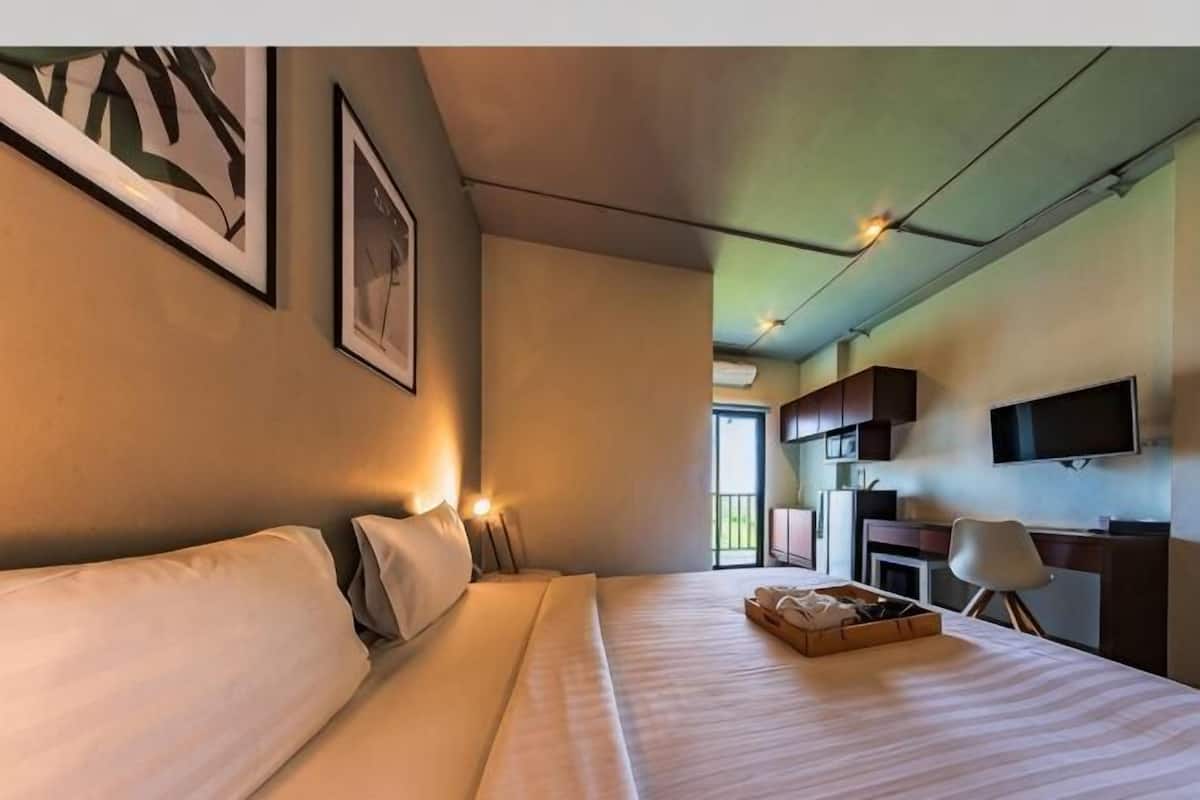 Ein Hotelzimmer mit Bett, Nachttisch, Kunstwerk, Fernseher und Fenster.