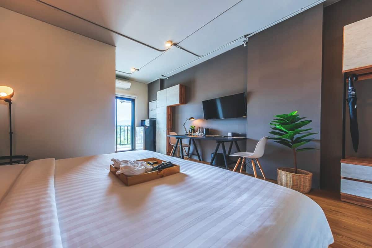 Ein modernes Hotelzimmer mit einem großen Bett, einem Schreibtisch mit Stuhl, einem Fernseher und einer Zimmerpflanze.