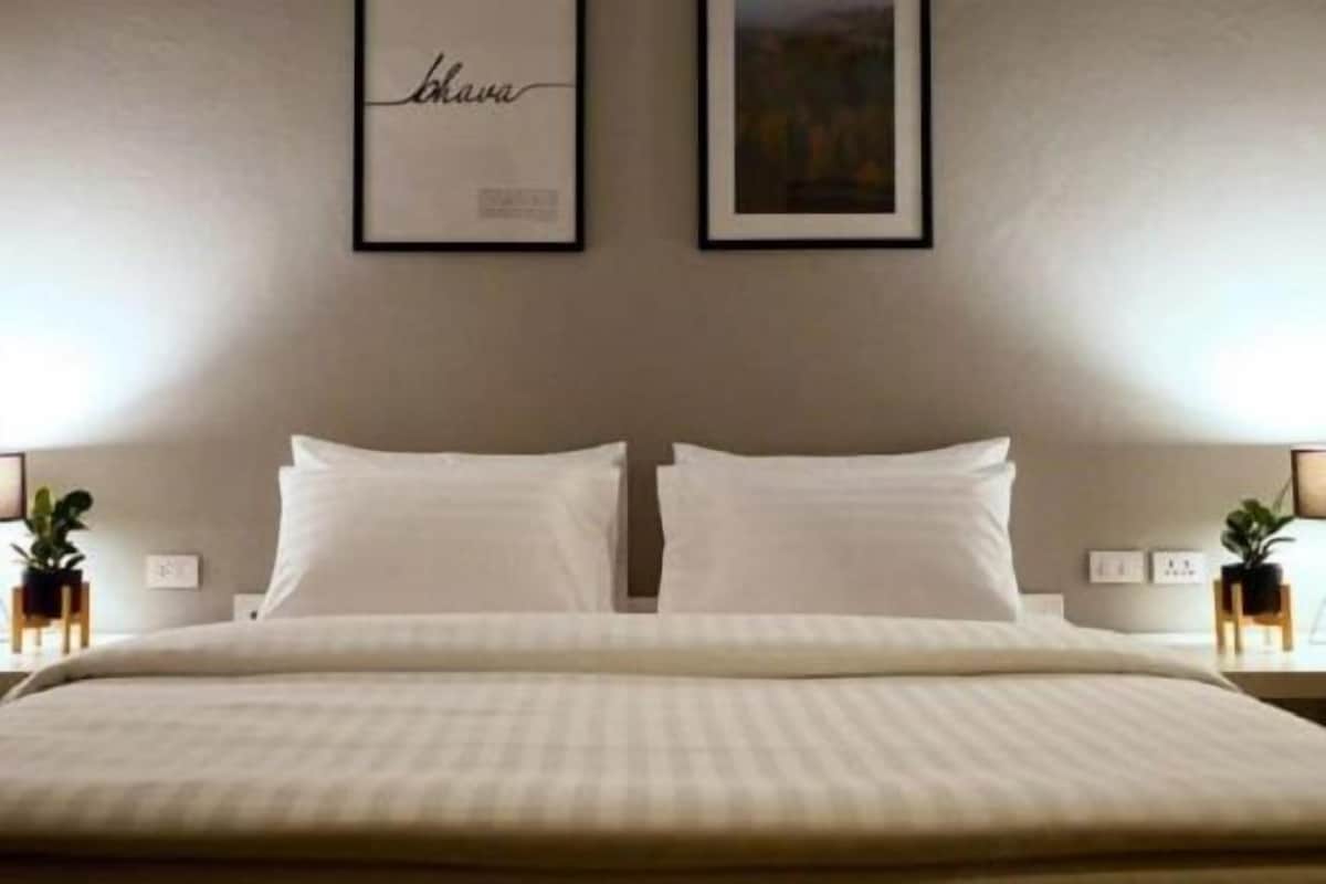 A neatly made bed with a striped bedspread, two framed pictures on the wall, and bedside tables with lamps and small potted plants.