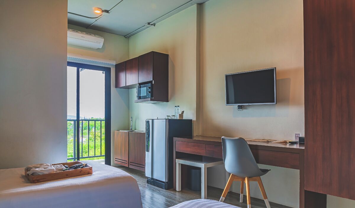 A compact hotel room with a bed, a desk, a chair, a TV, a microwave, and a refrigerator.