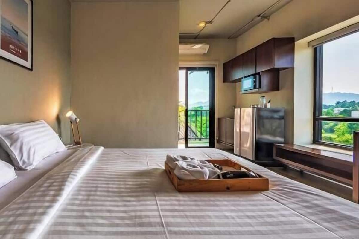 Ein Schlafzimmer mit Bett, Tablett mit Handtüchern, Fernseher, Kühlschrank und Balkon mit Blick.