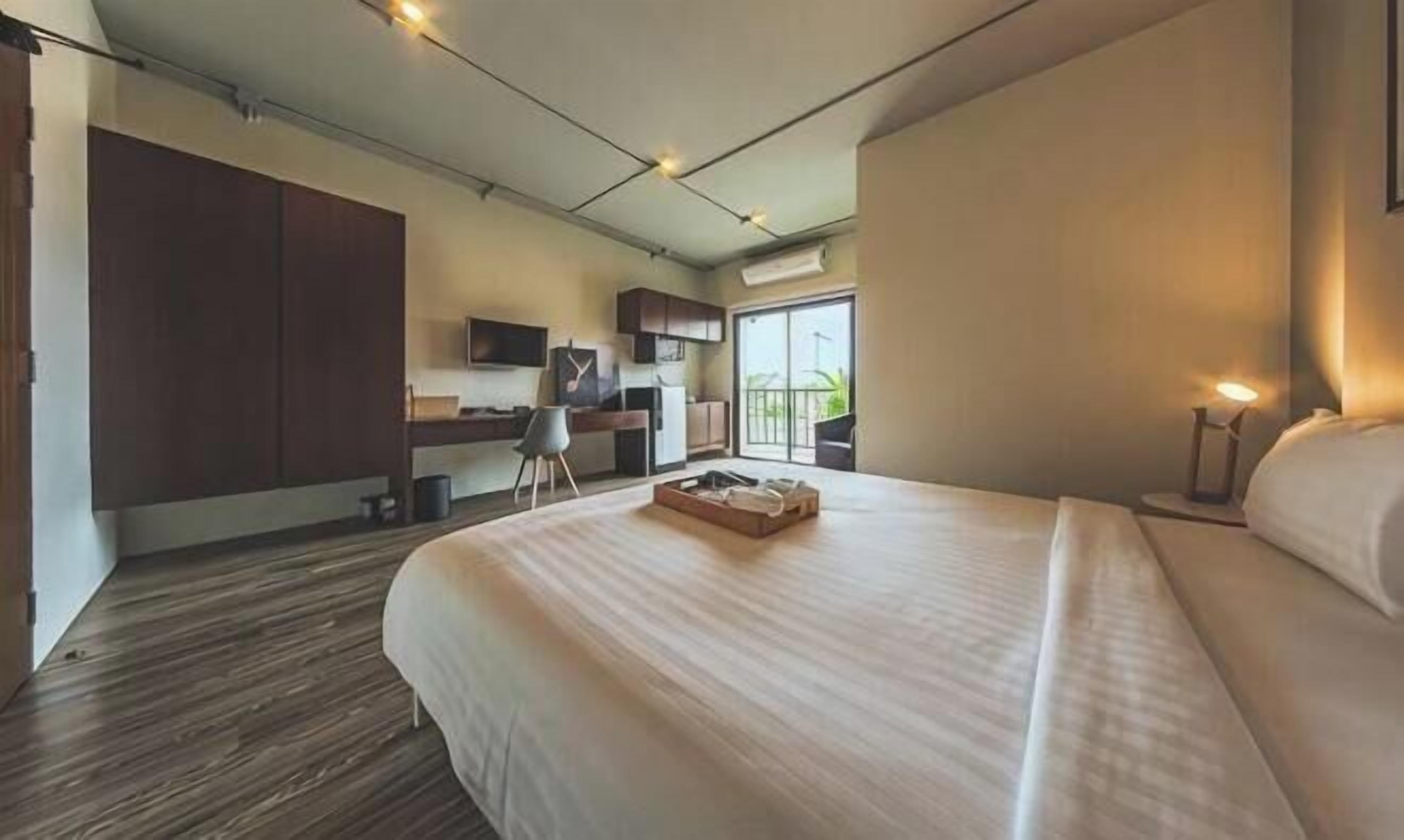 A modern hotel room with a large bed, a desk, and a kitchenette.