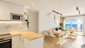 A modern kitchen with a built-in microwave, a dining area with a wooden table and chairs, and a balcony with a view of the sea. - MONACO 1 A Roses (Rosas / Roses)