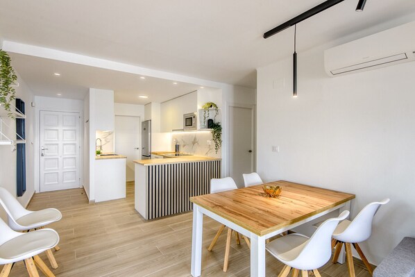 A modern kitchen with a central island, white chairs, and a wooden dining table.