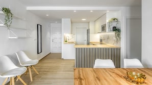 A modern kitchen with a central island, white chairs, and a wooden dining table. - MONACO 1 A Roses (Rosas / Roses)