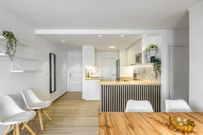 A modern kitchen with a central island, white chairs, and a wooden dining table.