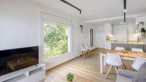 A modern living room with a flat-screen TV, a dining area with a wooden table and chairs, and a kitchen area with a countertop and sink. - MONACO 1 A Roses (Rosas / Roses)