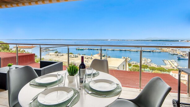 A dining area with a table set for two, overlooking a marina with boats and a clear blue sky. - MONACO 1 A Roses (Rosas / Roses)