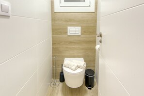 A small, modern bathroom with a toilet, a hand dryer, and a trash bin. - MONACO 1 A Roses (Rosas / Roses)