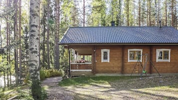 Een houten blokhut met een veranda, omgeven door een bos.