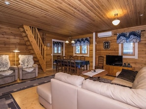 Een gezellig chaletinterieur met houten plafond, een bank, een eettafel met stoelen, een televisie en een open haard.