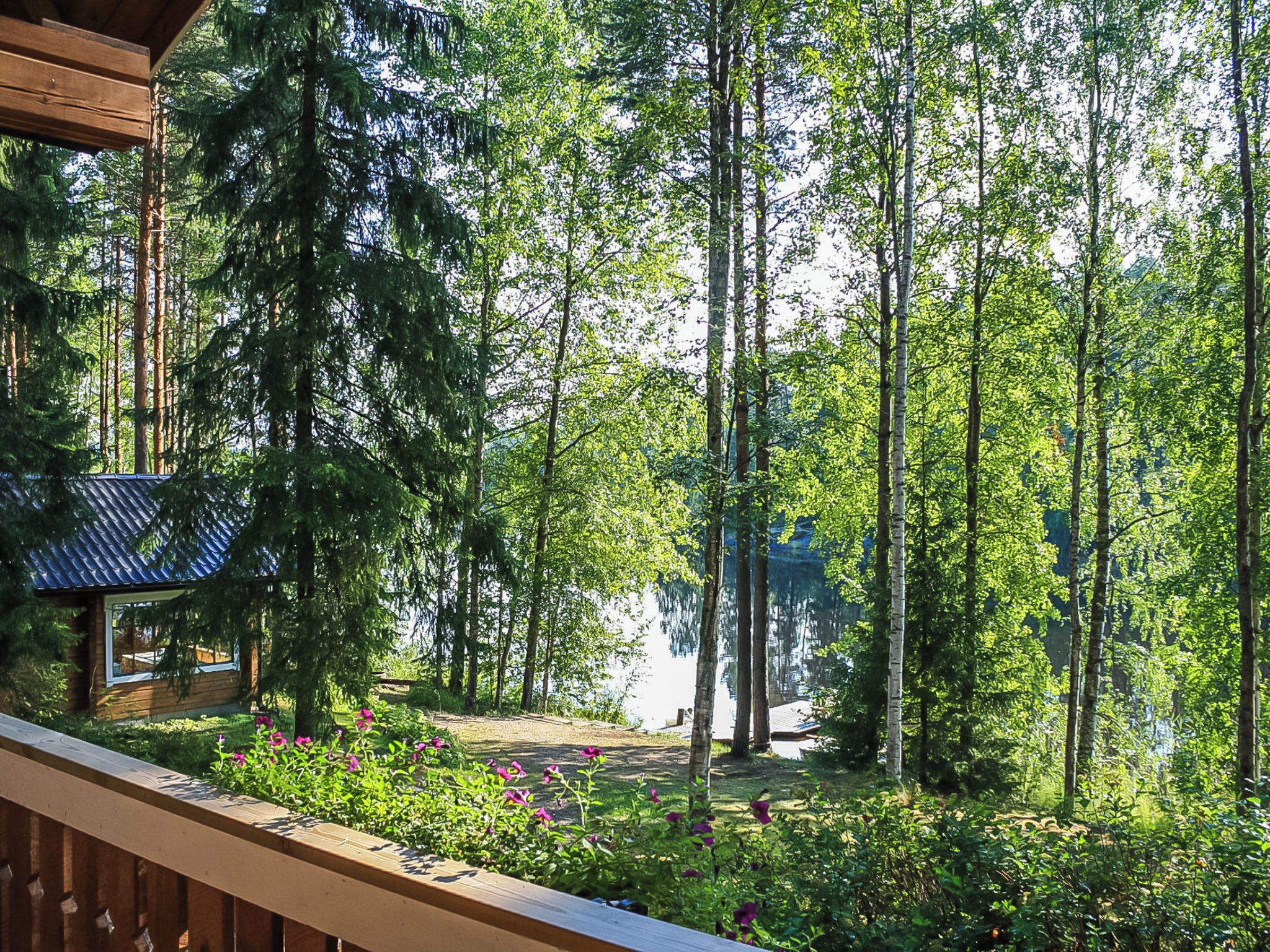 A wooden deck overlooking a forested area with a small cabin and a clear view of the surrounding trees.