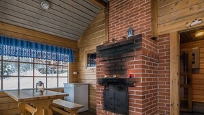 Een gezellig blokhut interieur met een metselwerk schoorsteen, houten wanden, een eettafel en een raam met uitzicht op besneeuwde bomen.
